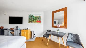 Una habitación de hotel con cama, escritorio, silla, televisor, cuadro y espejo.