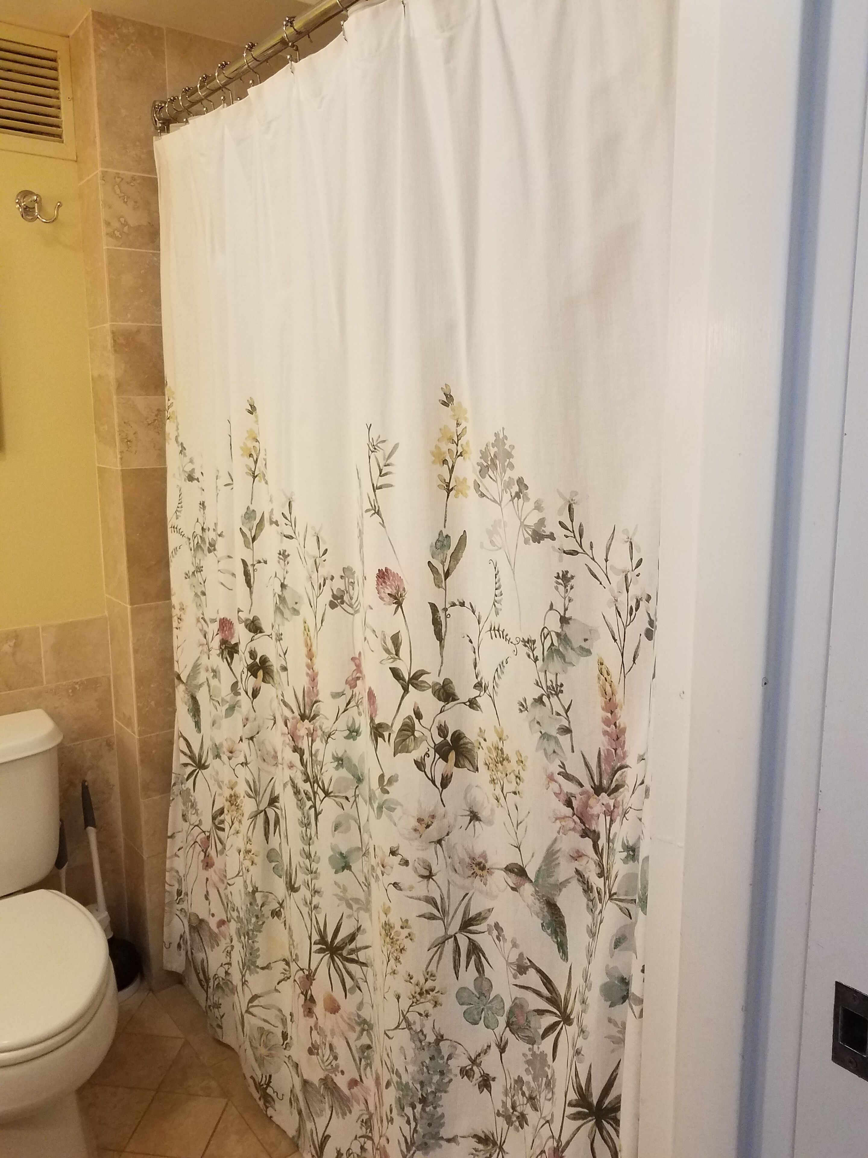 A bathroom with a floral shower curtain, a toilet, and a tiled wall.
