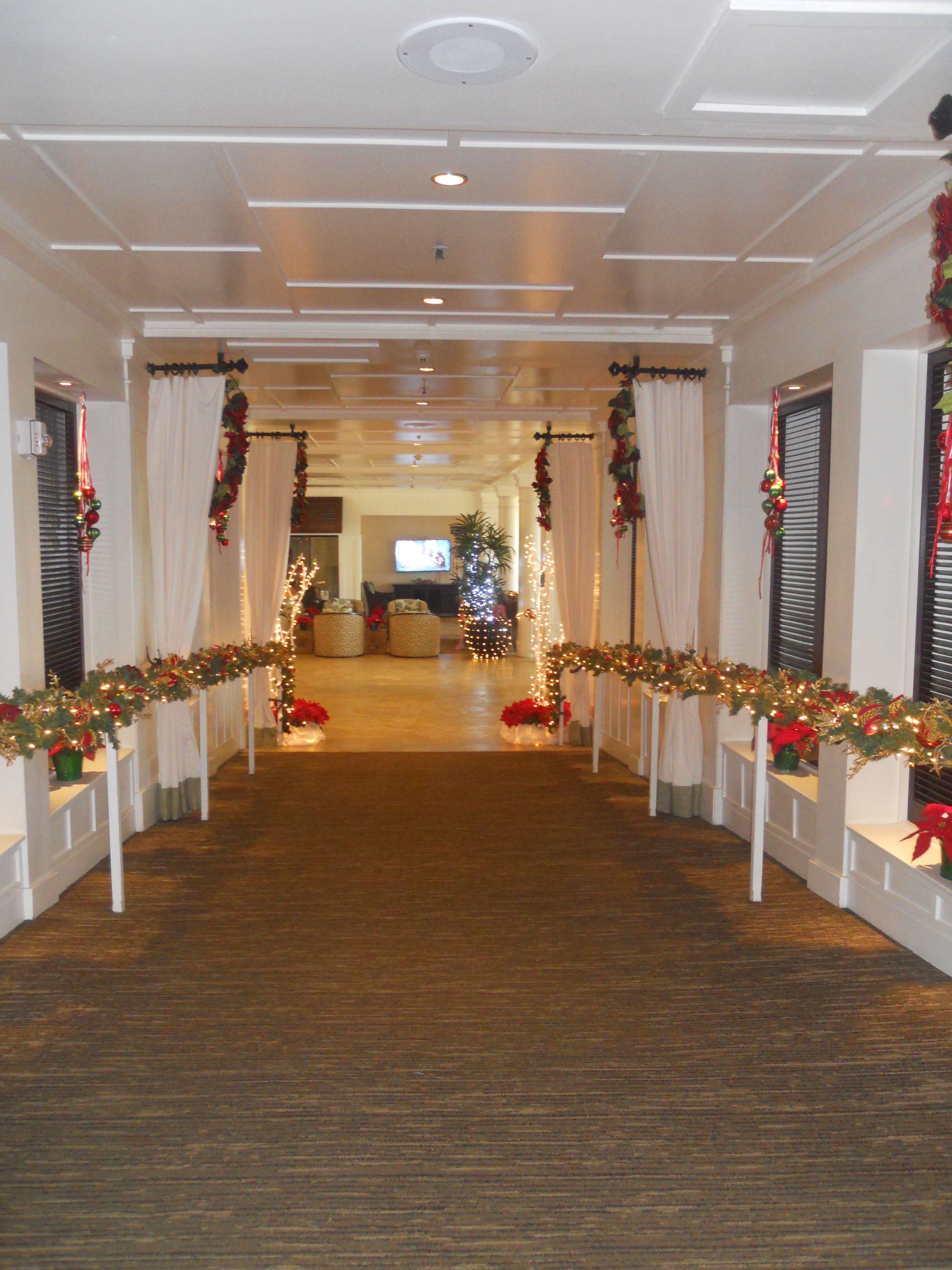 Un pasillo de hotel con suelo de madera, paredes blancas y un árbol de Navidad al fondo.