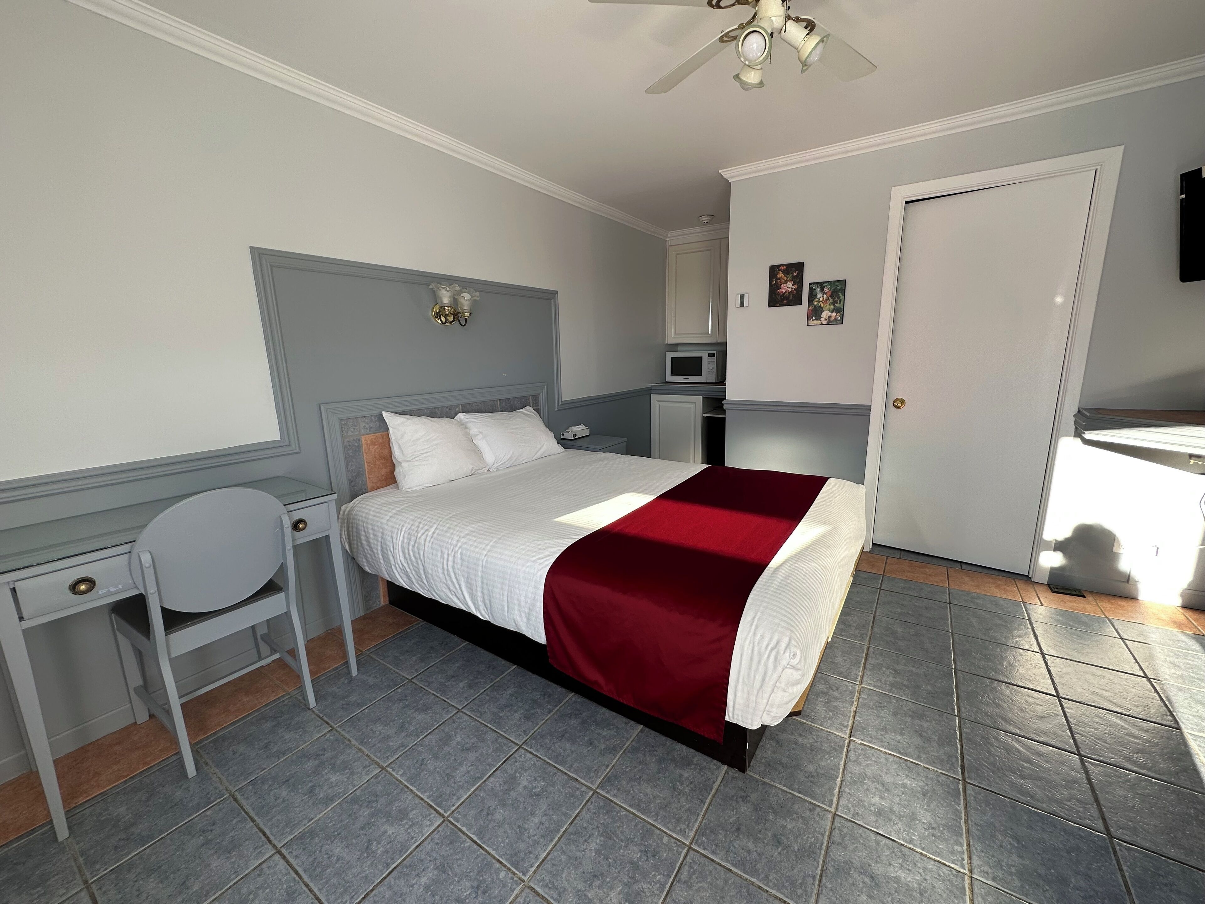 A bedroom with a bed, a desk, a chair, a microwave, and a door.