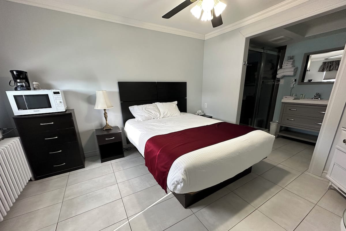 A hotel room with a bed, a nightstand with a lamp, a microwave, and a bathroom visible through an open door.