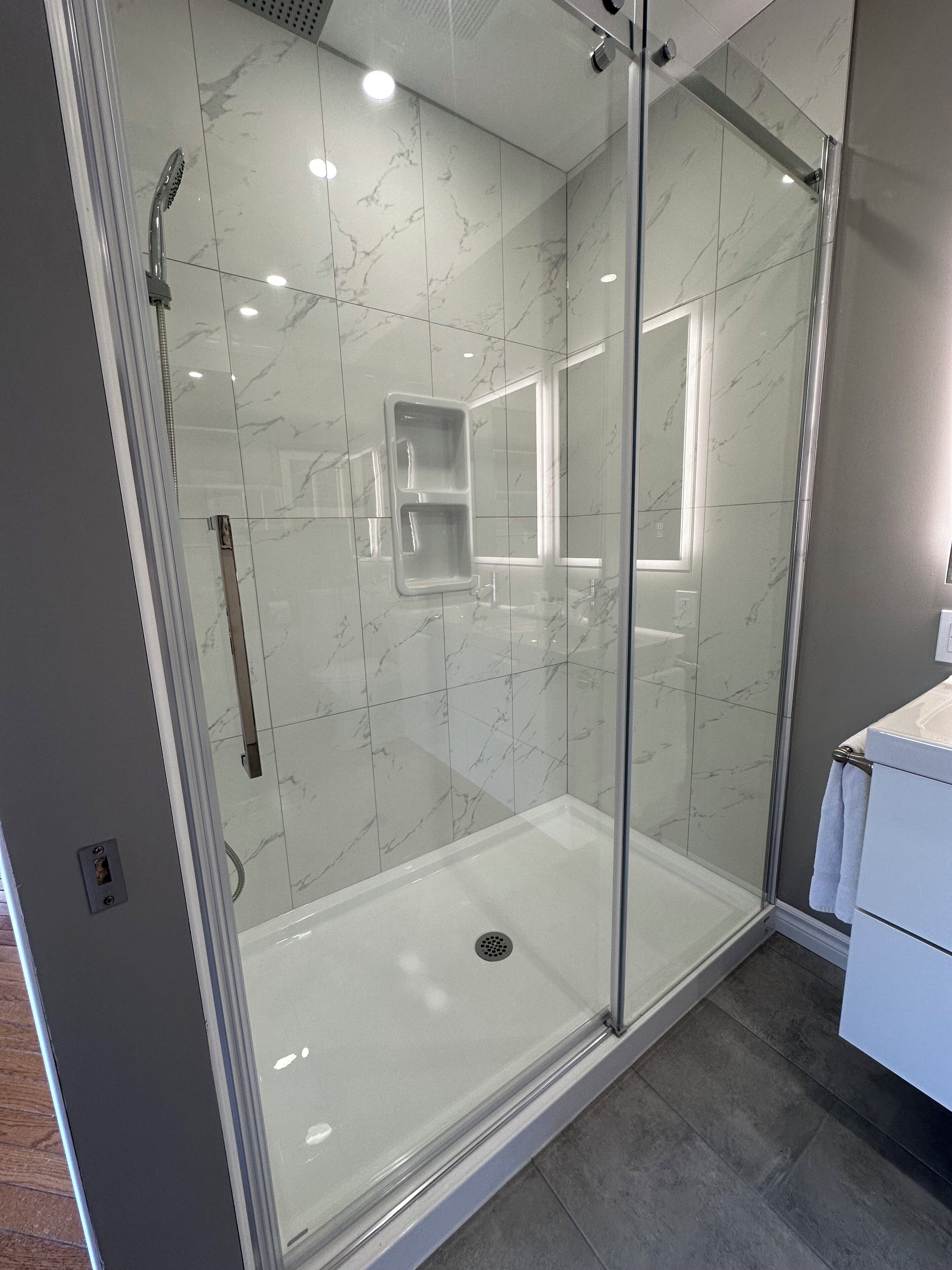 Un baño moderno con ducha de vidrio, azulejos de mármol y un lavamanos blanco.