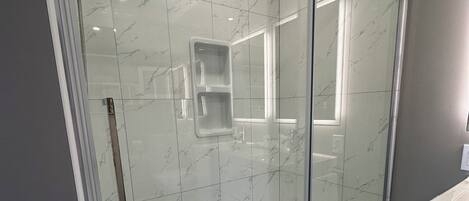 Un baño moderno con ducha de vidrio, azulejos de mármol y un lavamanos blanco.