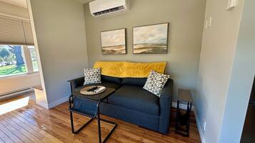 A living room with a grey sofa, two patterned pillows, a yellow throw, and a coffee table with remote controls.