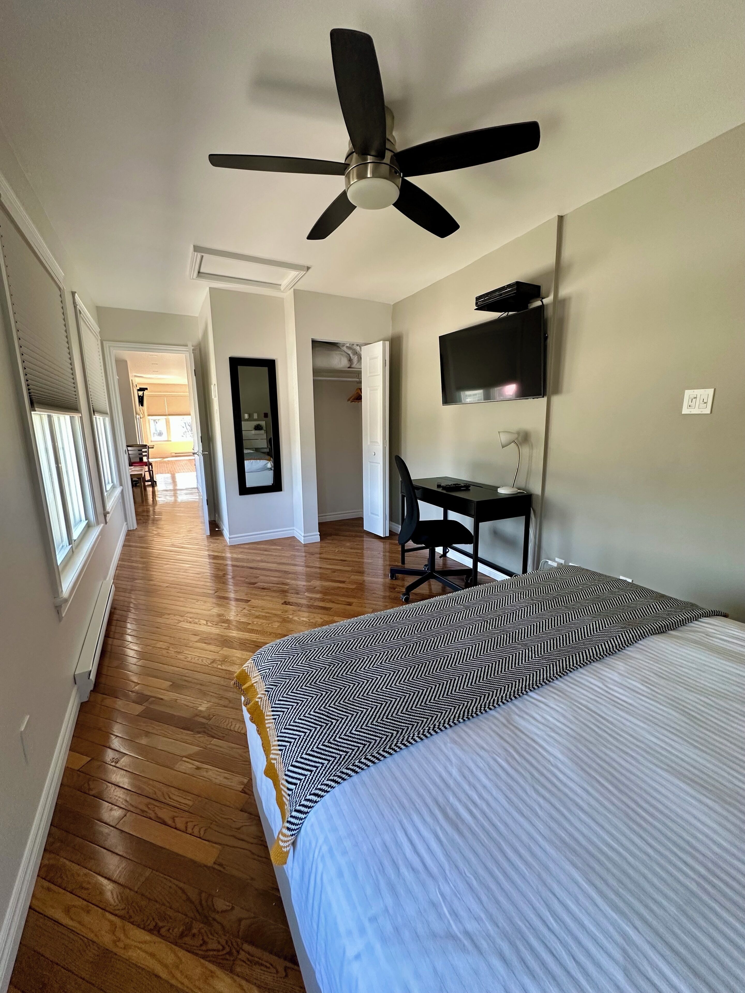 A hotel room with a bed, a desk, a chair, a TV, and a ceiling fan.
