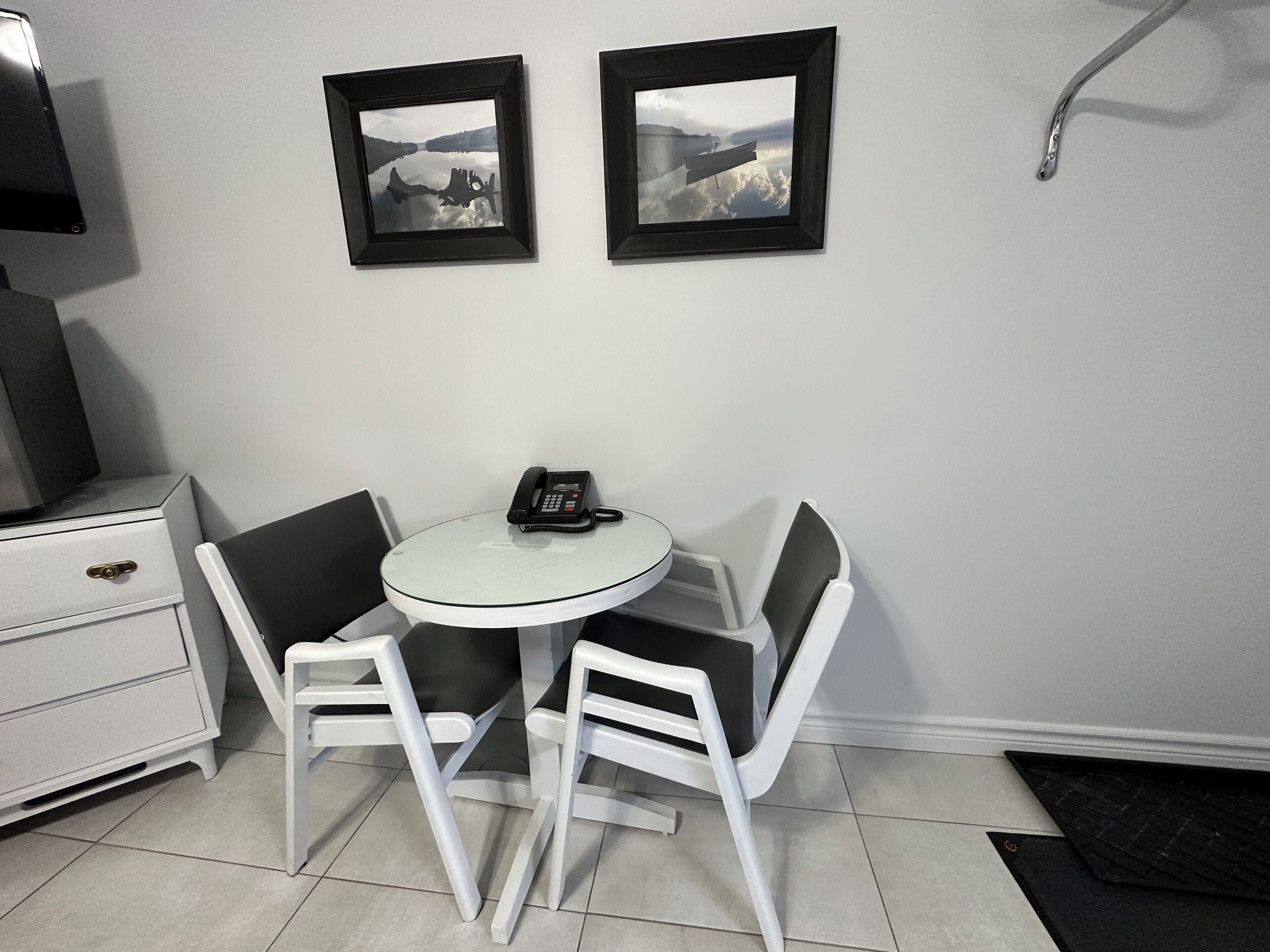 Una habitación pequeña y moderna con una mesa redonda, dos sillas, un teléfono y dos cuadros en la pared.