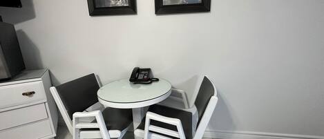 Una habitación pequeña y moderna con una mesa redonda, dos sillas, un teléfono y dos cuadros en la pared.