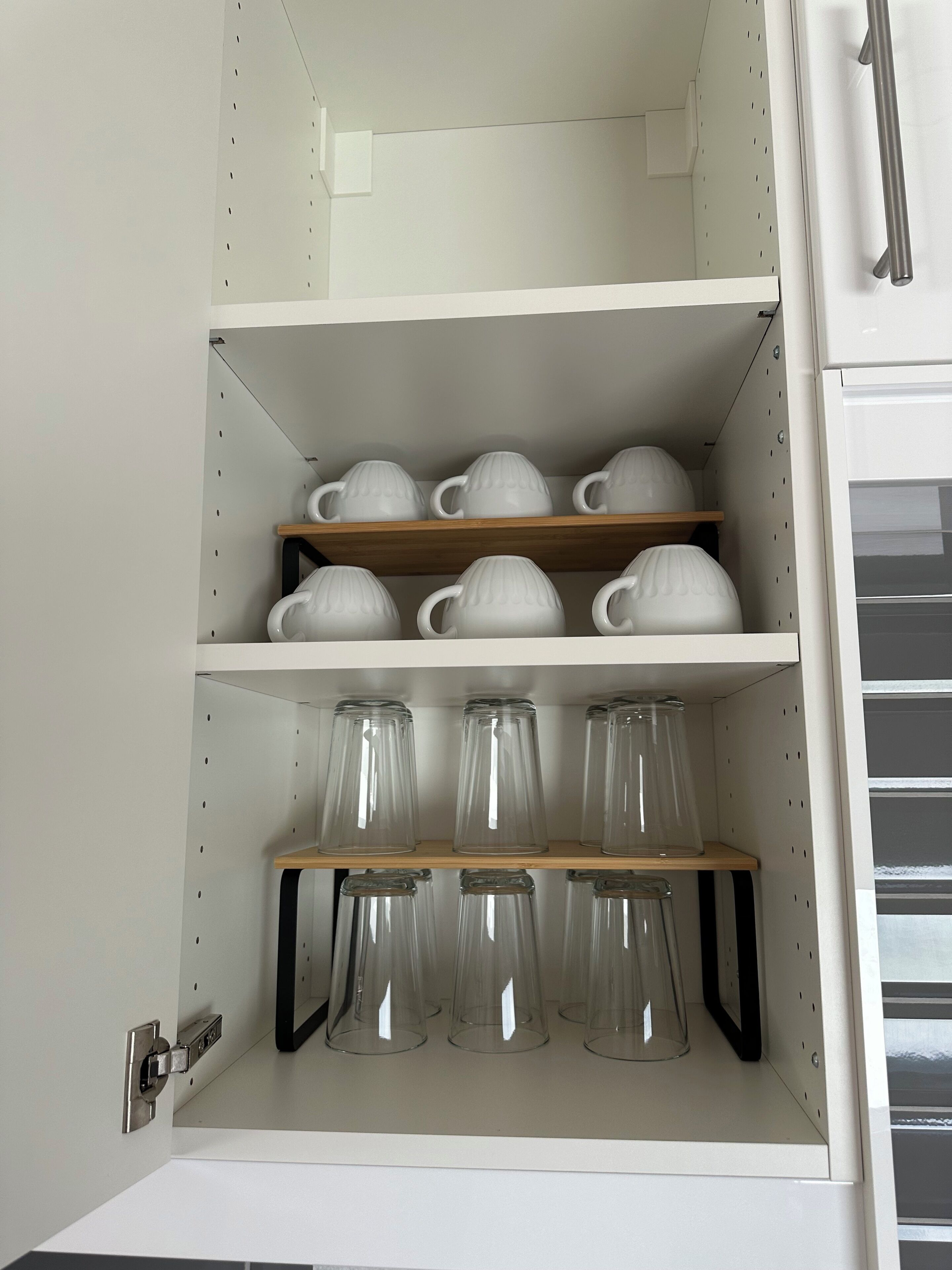 Een keukenkast met planken waarop witte theepotten en glazen bekers staan.