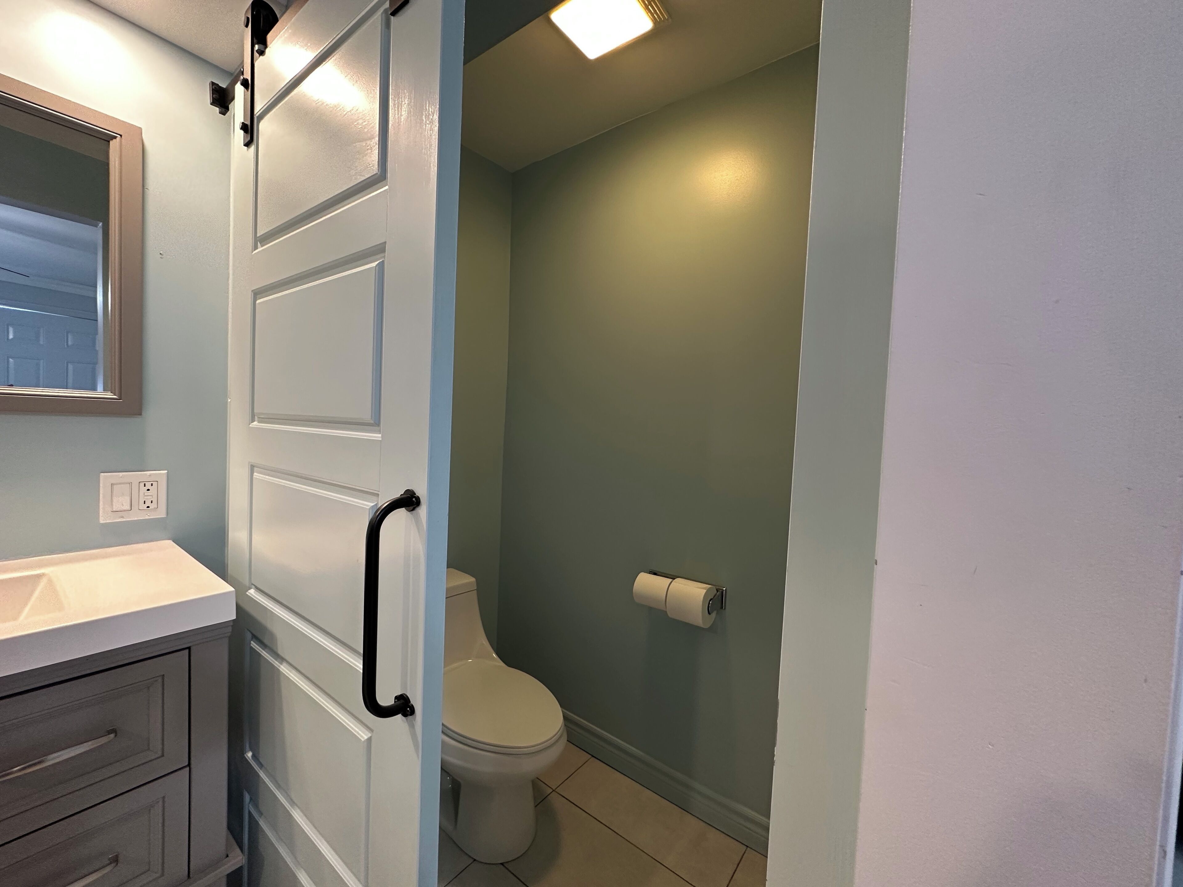 A bathroom with a white toilet, a towel dispenser, and a sink with a mirror above it.