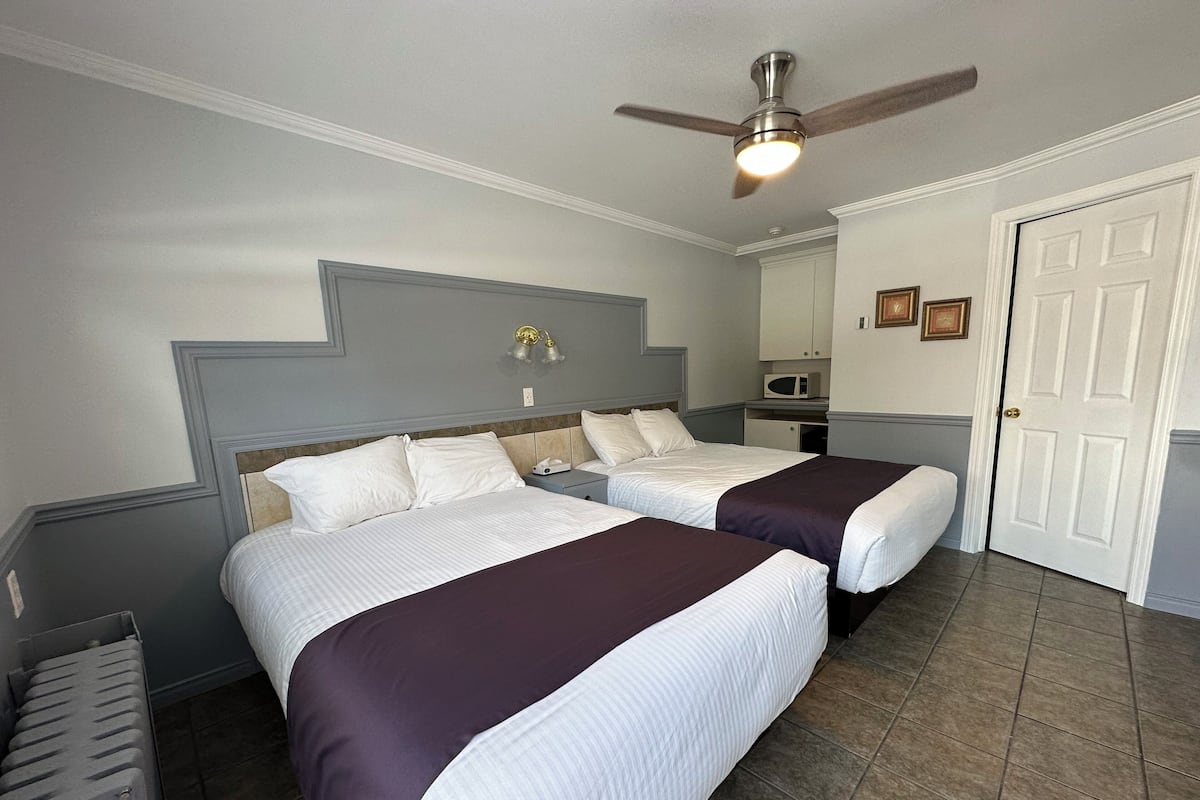 A hotel room with two beds, a ceiling fan, a microwave, and a door.