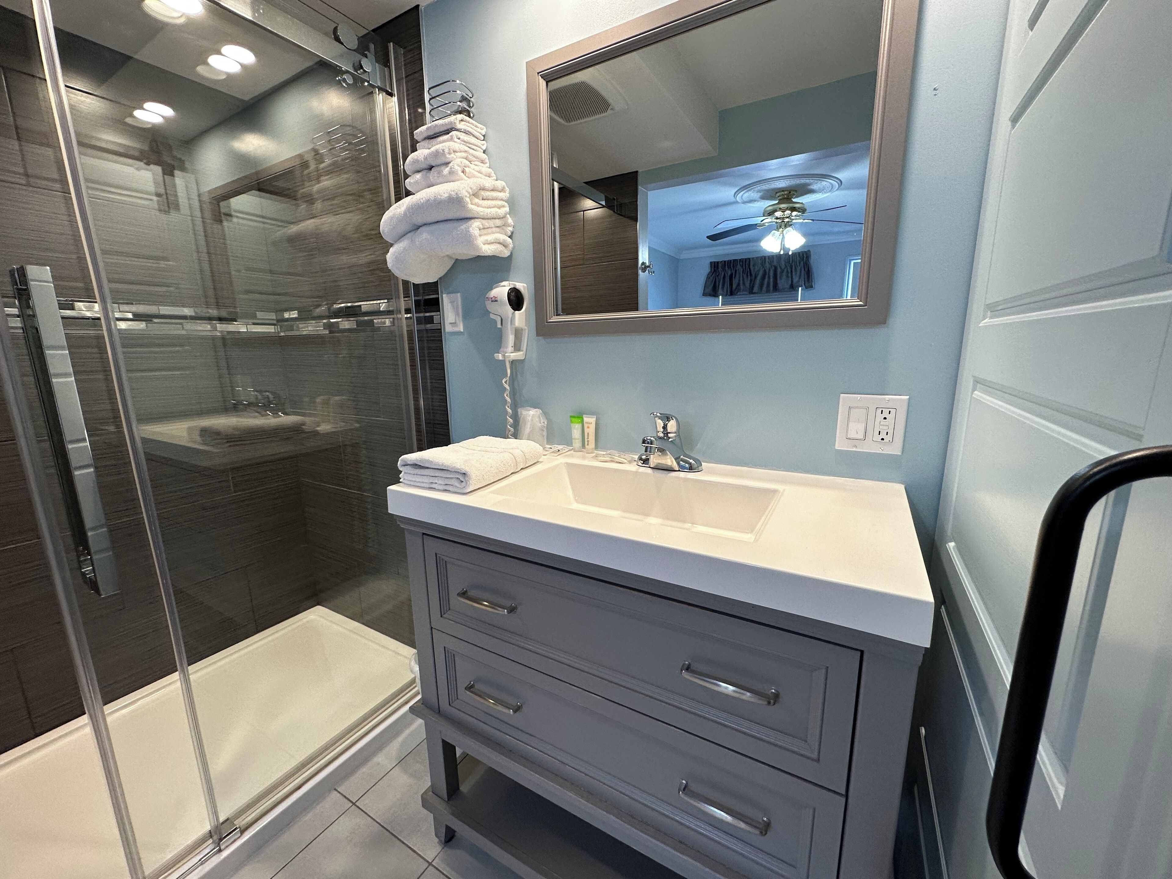 Un baño moderno con cabina de ducha de vidrio, un lavabo blanco y un mueble con cajones.