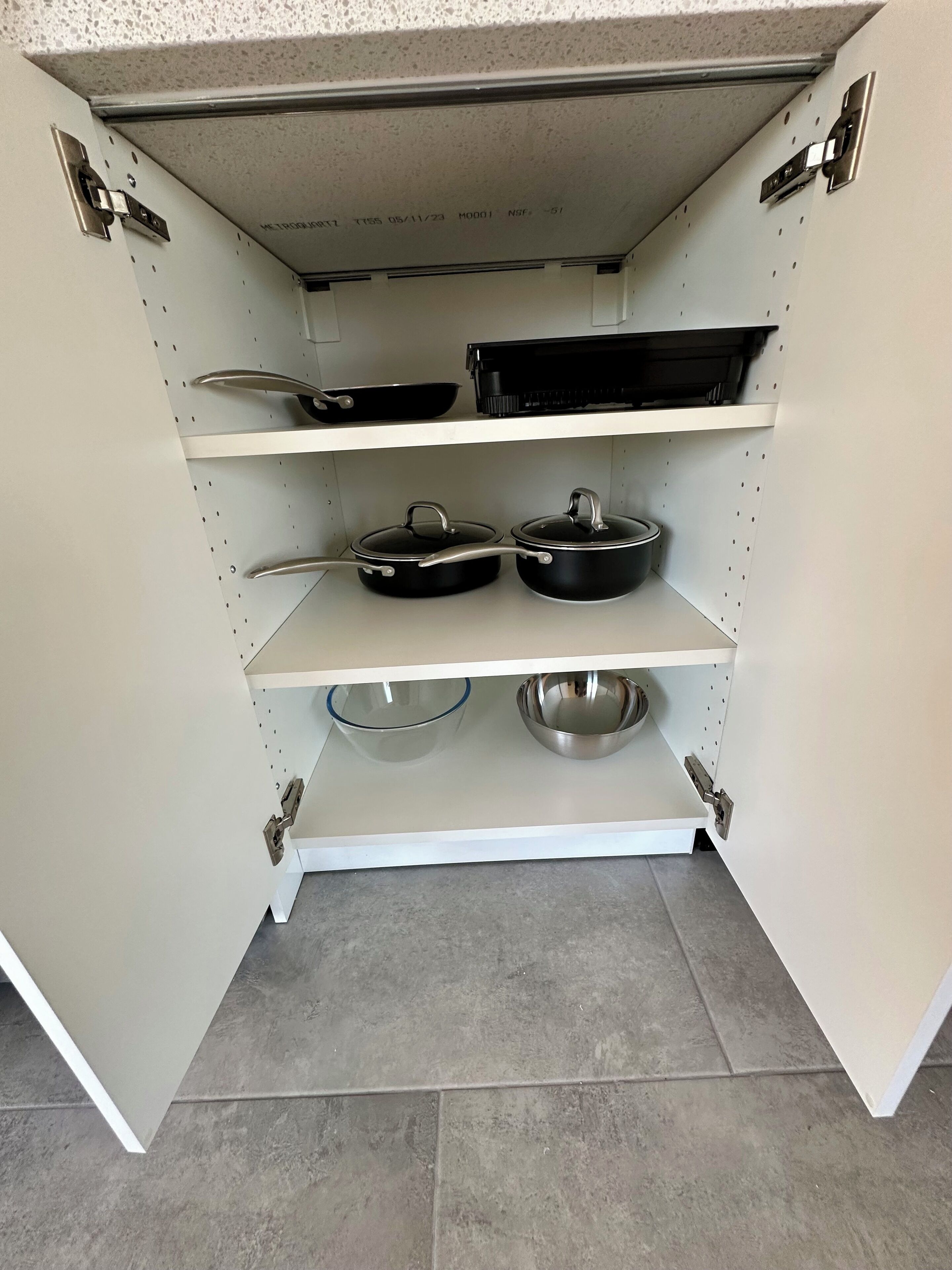 A kitchen cabinet with pots, pans, and a frying pan.