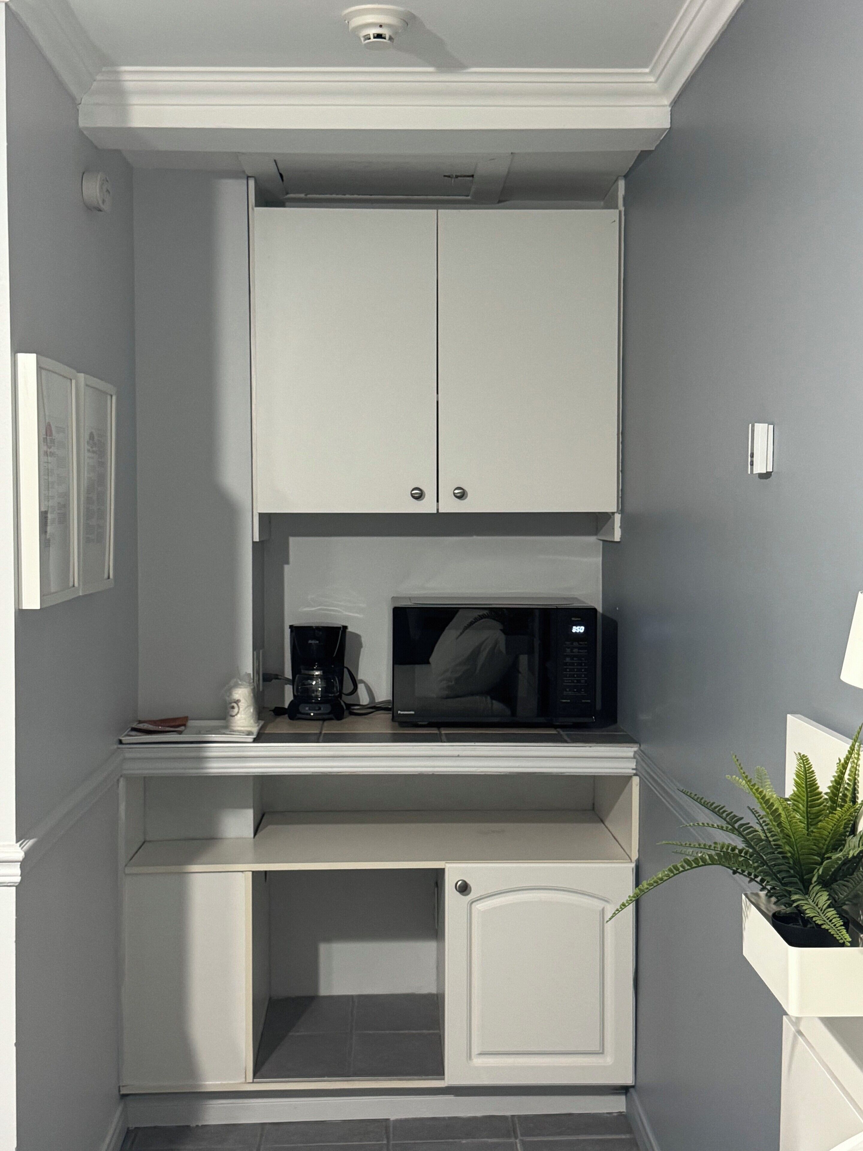A compact kitchen with white cabinetry, a microwave, and a coffee maker.