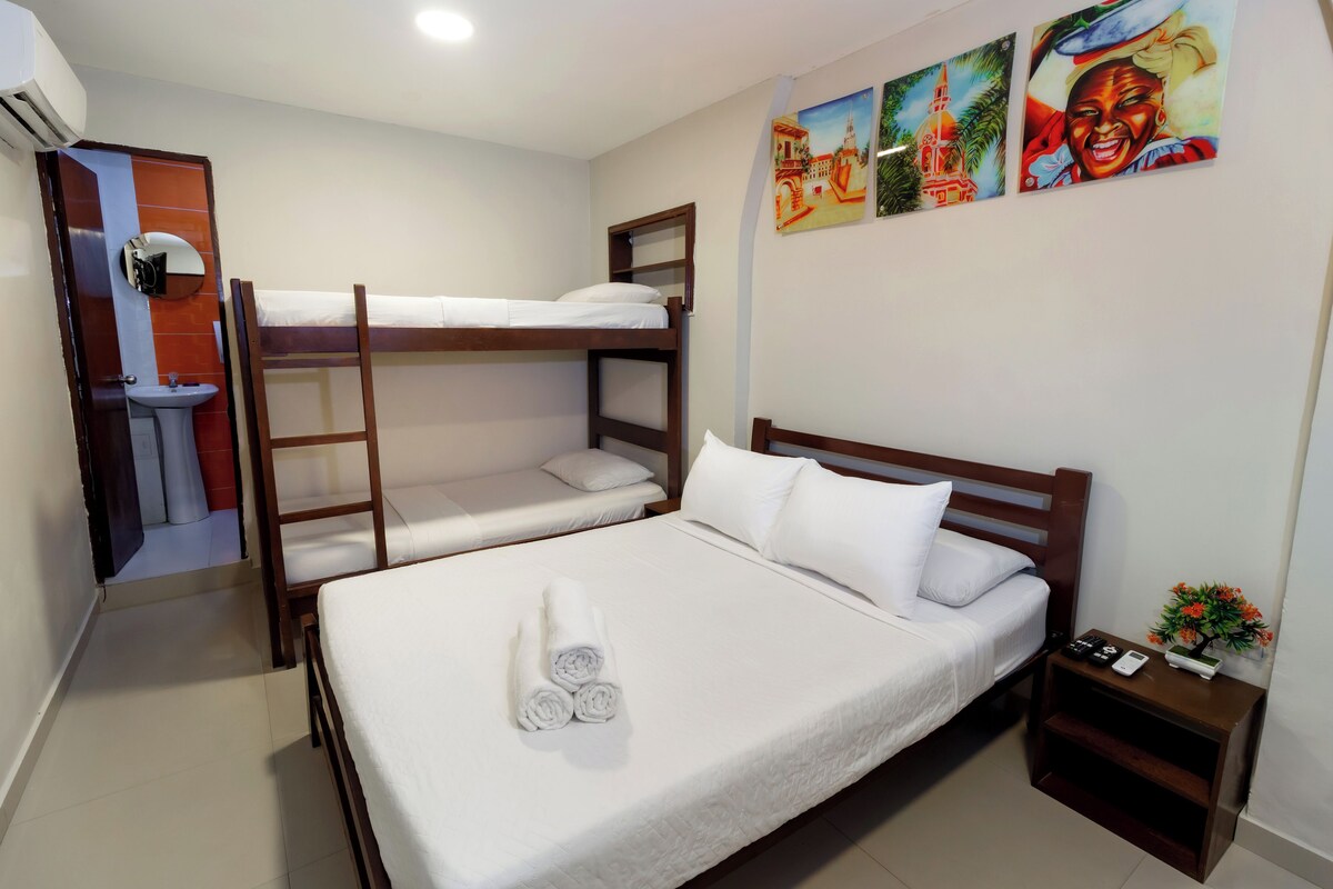 A hotel room with bunk beds, a sink, a mirror, and a nightstand with a remote control.