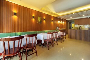 L’intérieur d’un restaurant présente des murs lambrissés en bois, des banquettes rembourrées de couleur verte et une longue table à manger entourée de chaises.