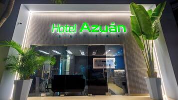 A entrada do Hotel Azuan, com design moderno, apresenta fachada de vidro e letreiros iluminados.