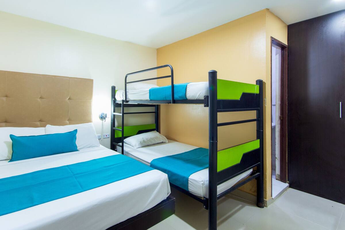 A hotel room with a bunk bed, a single bed, and a wooden headboard.