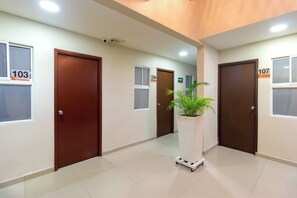 A hallway with doors numbered 103 and 107, a potted plant, and a cart. - Hotel Azuan Suites By Geh Suites (Cartagena)