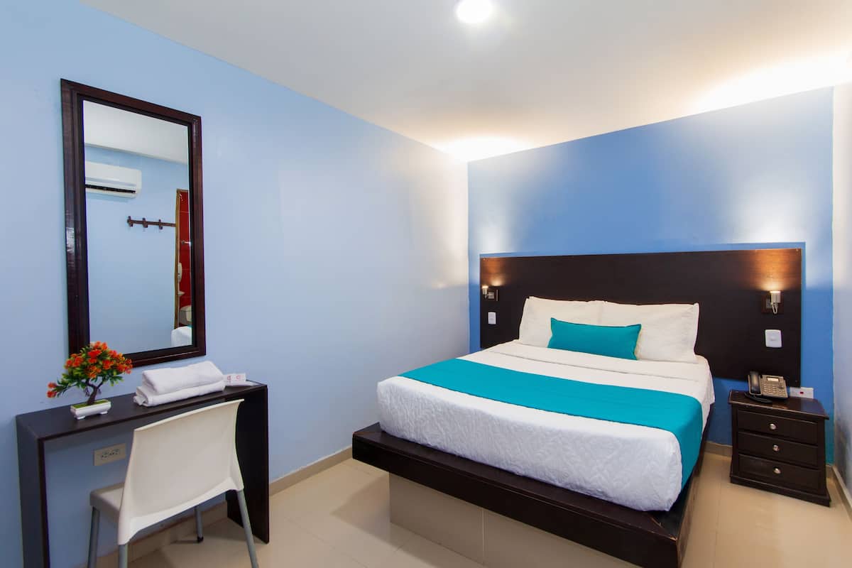 A hotel room with a bed, bedside table, nightstand, desk, chair, and a mirror.
