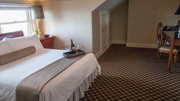 A hotel room with a large bed, a desk, and a chair. There is a window with a view of the outside.