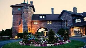 A large stone building with a prominent tower and an arched entrance, surrounded by a well-maintained garden.