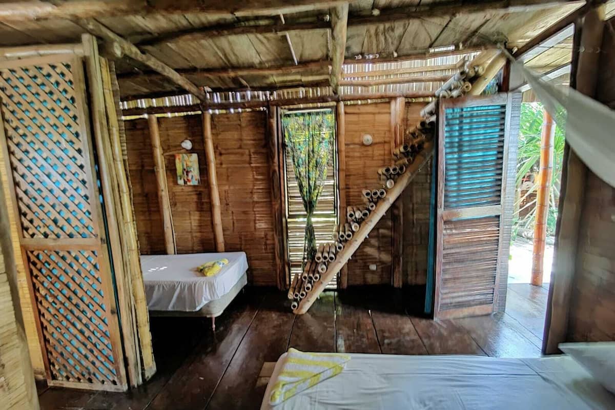 Una habitación rústica de madera con una cama, una mesita y una escalera que lleva a un balcón.