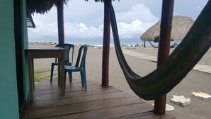 A wooden deck with a table and chairs, a hammock, and a thatched umbrella.