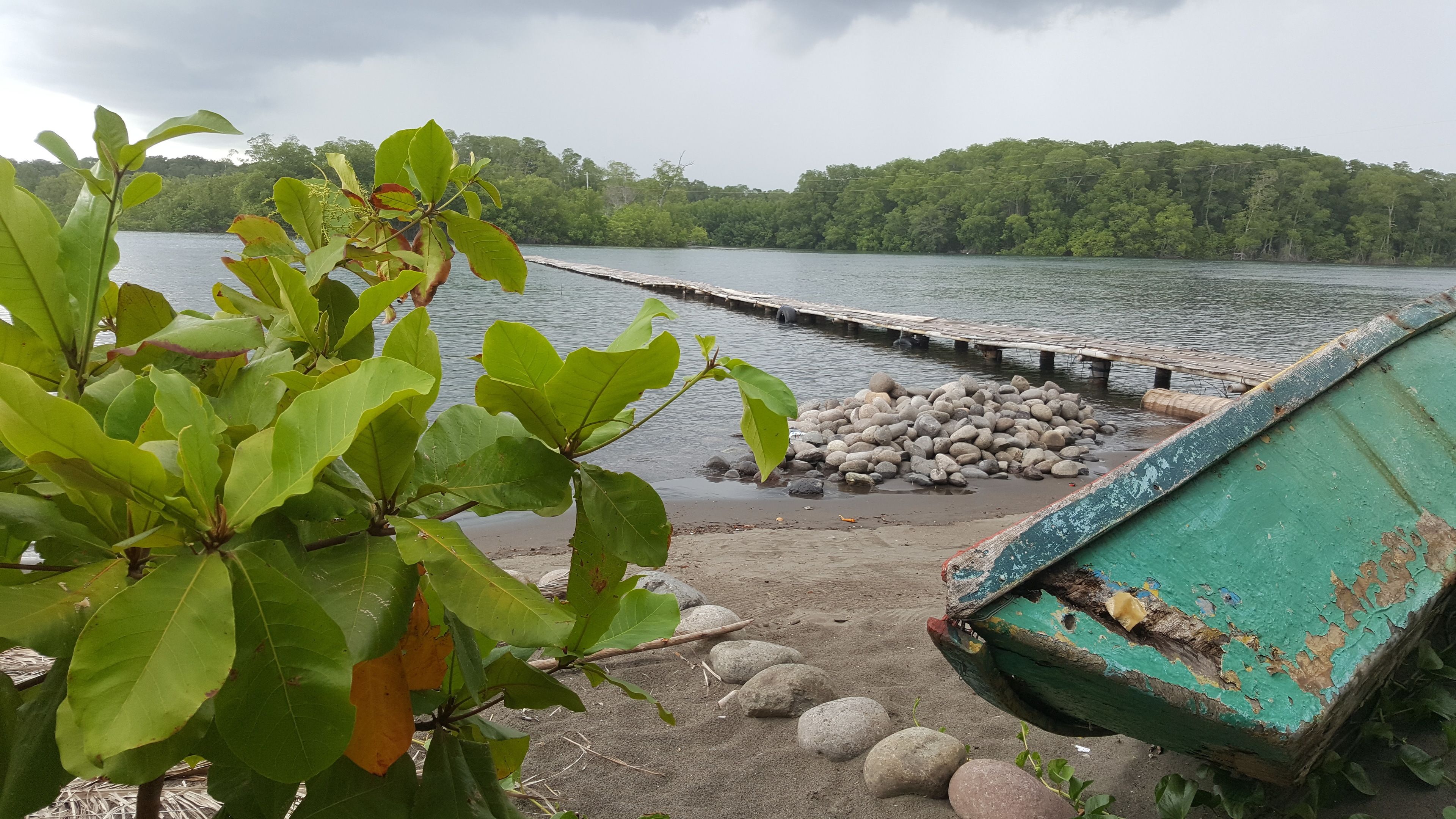 Un muelle que se adentra en un lago tranquilo, con una orilla boscosa al fondo.