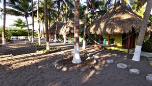 A beach area with thatched-roof huts, palm trees, and a hammock.
