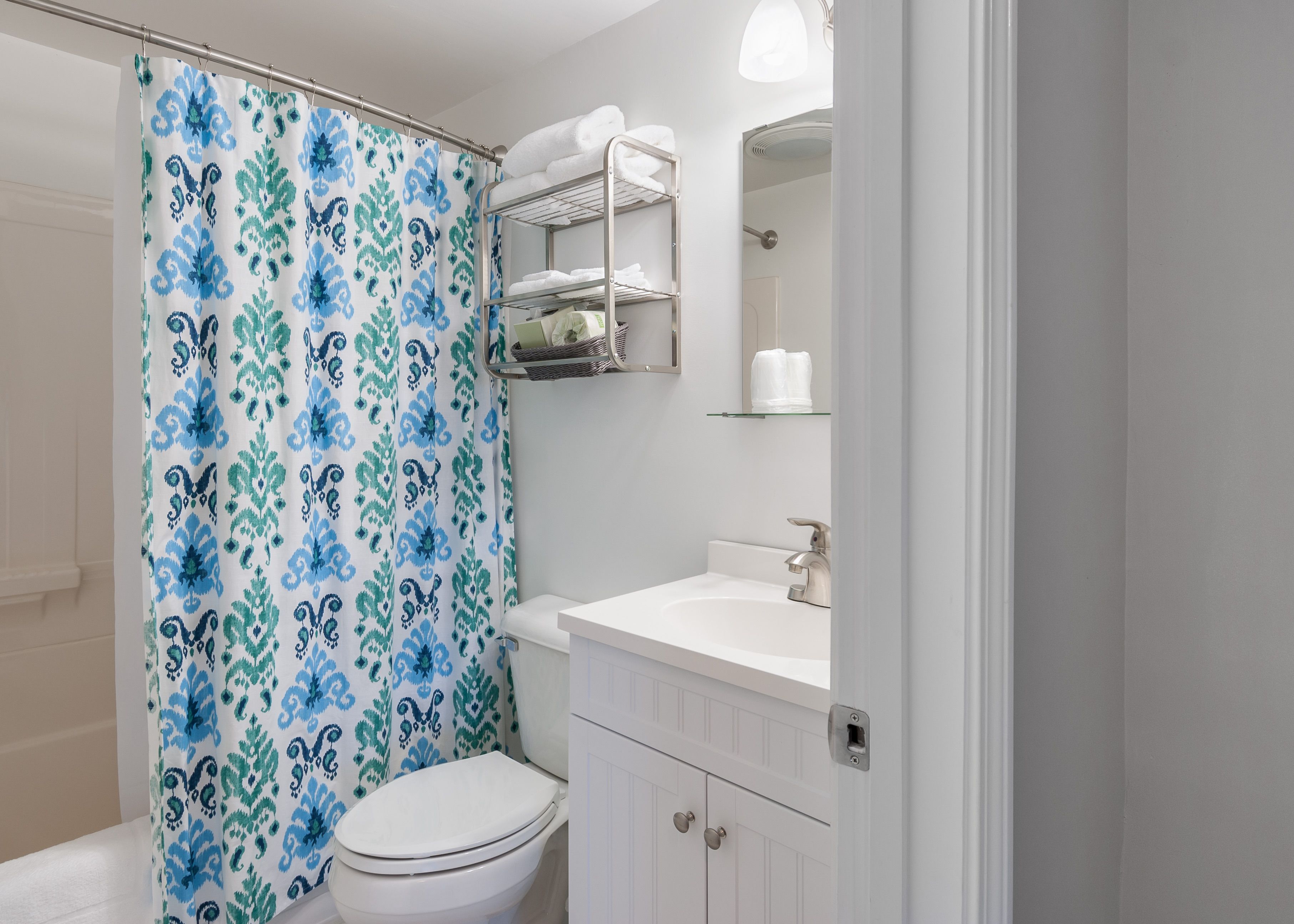 A bathroom with a shower curtain, a toilet, a sink, and a mirror.