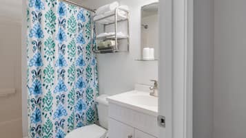 A bathroom with a shower curtain, a toilet, a sink, and a mirror.