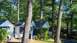 A two-story cabin with a porch and outdoor seating, surrounded by tall trees.