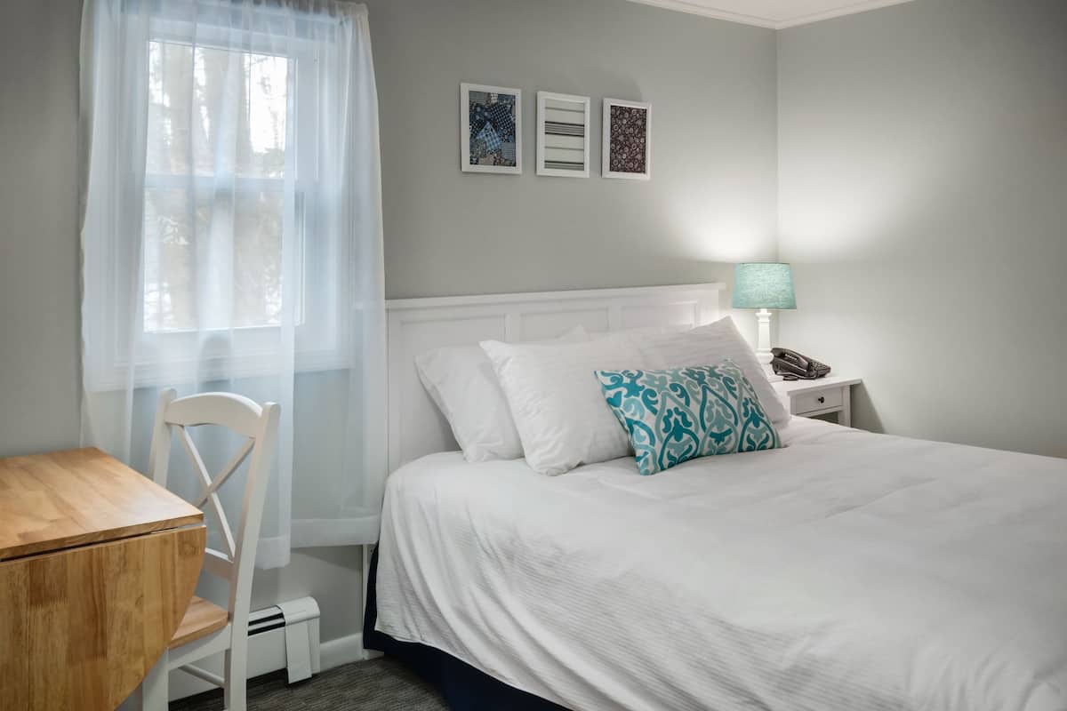 A bedroom with a bed, a bedside table, a lamp, a chair, and a small table.