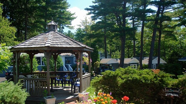 A gazebo with a tiled roof, surrounded by a brick pathway and colorful flowers.