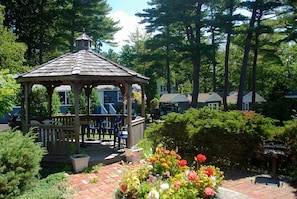 A gazebo with a tiled roof, surrounded by a brick pathway and colorful flowers. - Kittery Inn and Suites (Kittery)