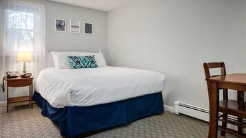 Habitación de hotel con una cama, una mesita de noche con lámpara, una silla y un cuadro con dos imágenes enmarcadas.