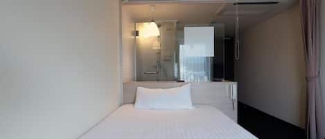 A hotel room with a bed, a bedside table, a mirror, and a window with curtains.