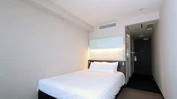 A hotel room with a single bed, a nightstand, a wall-mounted lamp, and a door leading to another room.