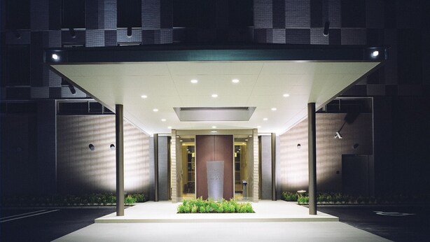 Una entrada de hotel moderna con un corredor cubierto, puertas de cristal y una fachada bien iluminada.