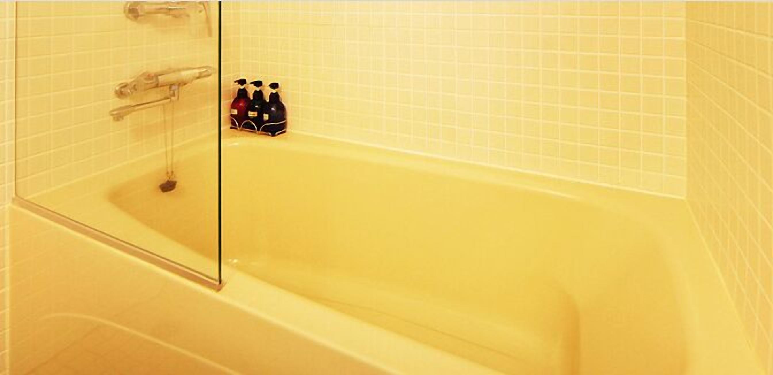 A bathtub with a glass door, a showerhead, and three bottles of shampoo.