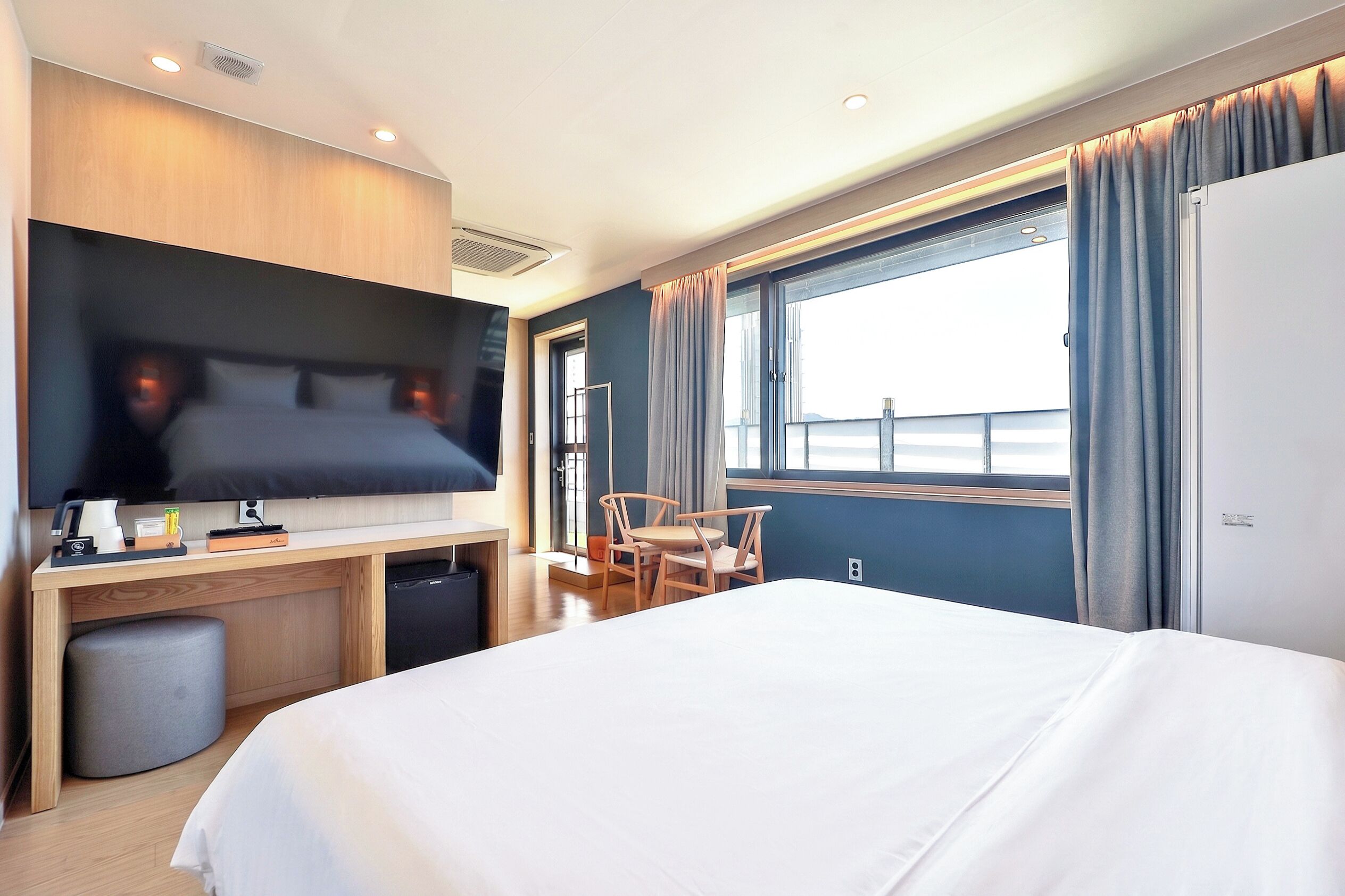 Ein Hotelzimmer mit einem Bett, einem Schreibtisch, einem Flachbildfernseher, einem Sessel und einem fenster mit Vorhängen.
