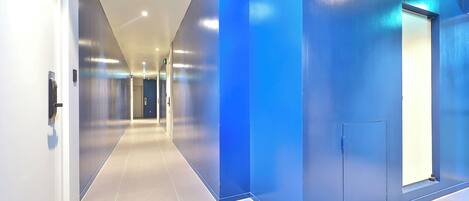 Un pasillo moderno con una pared azul decorativa, una puerta con picaporte y un accesorio de iluminación en el techo.