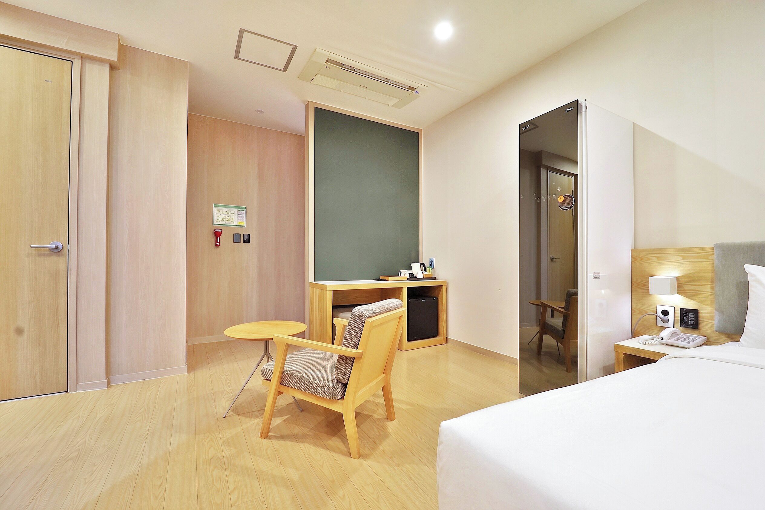A hotel room with a bed, a desk with a chair, a small table, and a wardrobe.