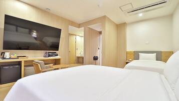 Habitación de hotel con cama, escritorio con televisor, refrigerador pequeño y baño con lavamanos y espejo.