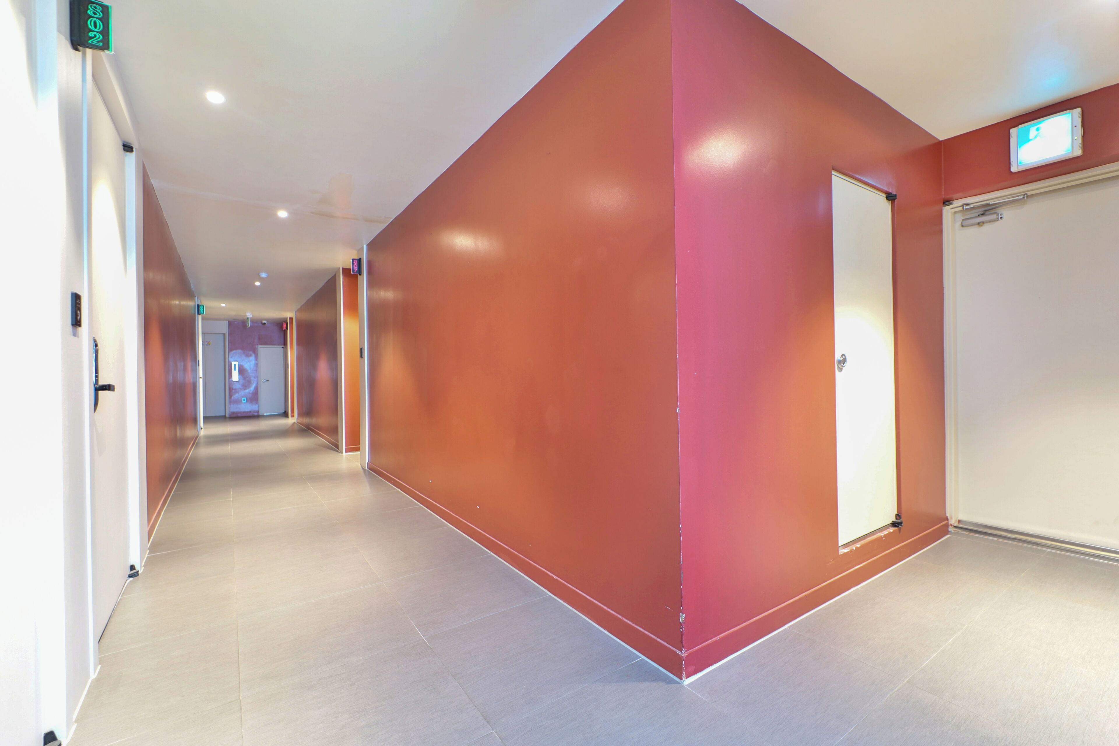 A corridor with a red wall and a white door at the end.