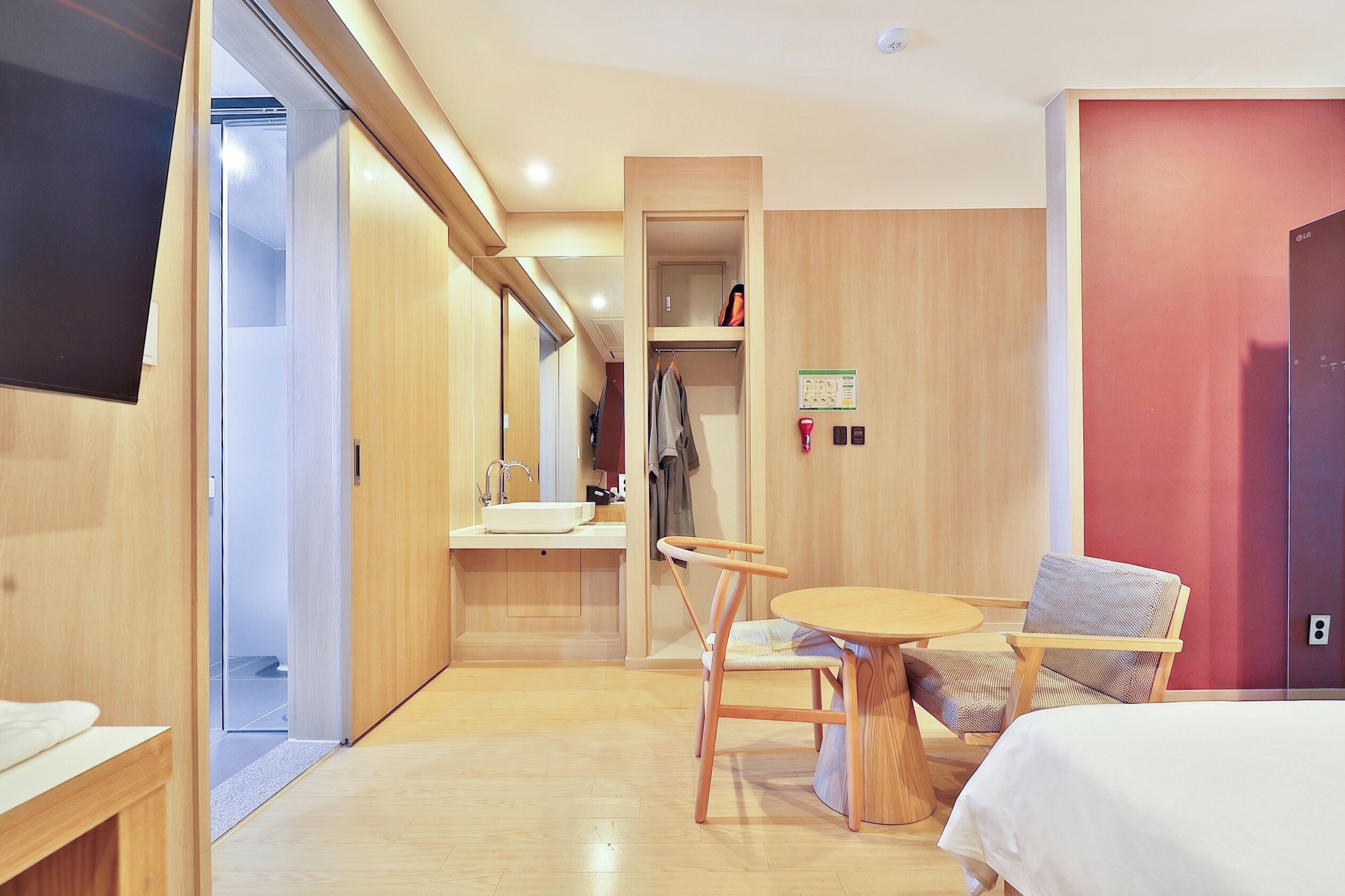 A hotel room with a bed, a small table, a chair, a sink, and a mirror.