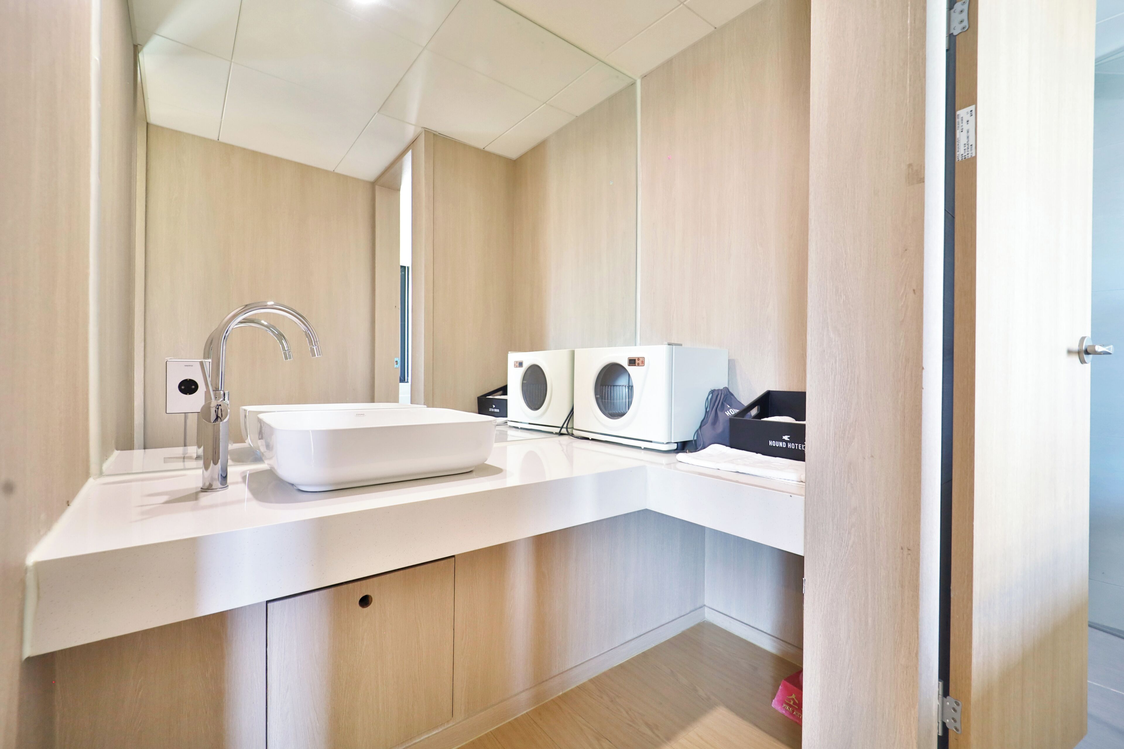 A modern bathroom with a white sink, a chrome faucet, and two wall-mounted washing machines.