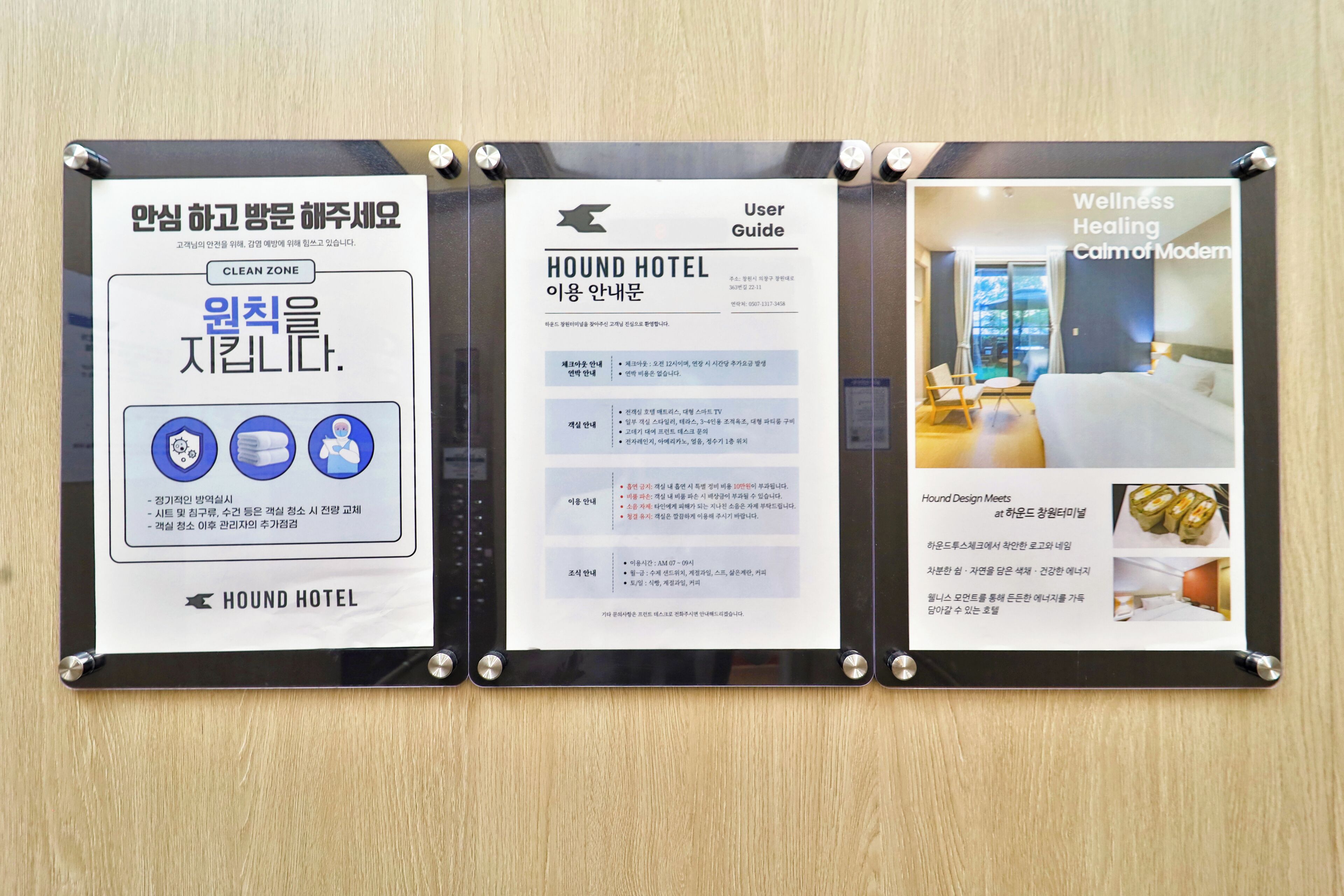 A bulletin board with three informational posters. The left poster is titled 'Clean Zone' and includes icons for cleanliness and hygiene. The middle poster is a 'User Guide' for Hound Hotel, detailing amenities and services. The right poster advertises 'Wellness Healing Calm of Modern' with images of a bed and food.