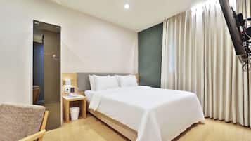 A hotel room with a bed, bedside table, lamp, chair, and a view of the outside through curtains.