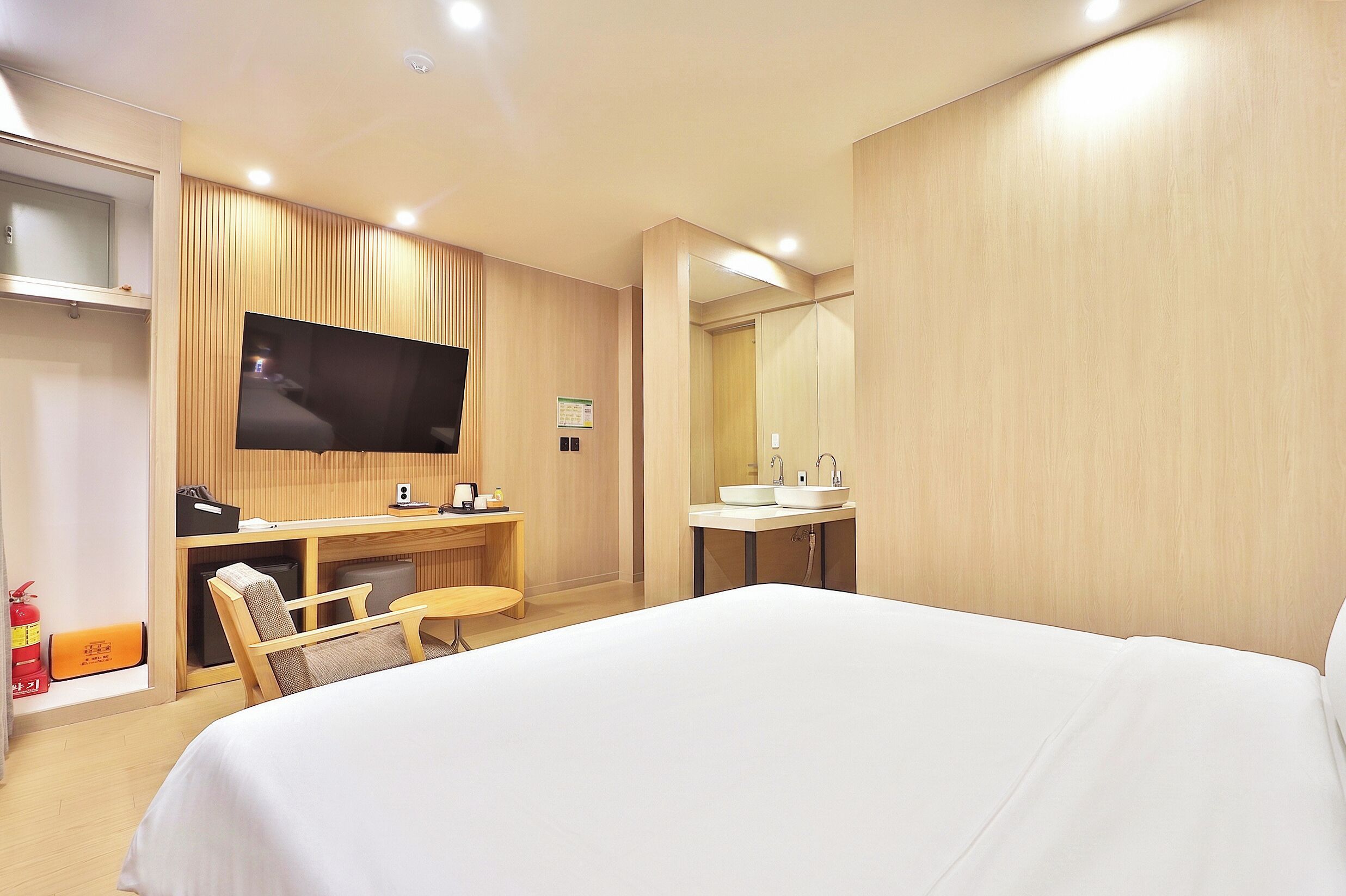 Quarto de hotel com uma cama, uma escrivaninha com cadeira, televisão, espelho e banheiro com pia.